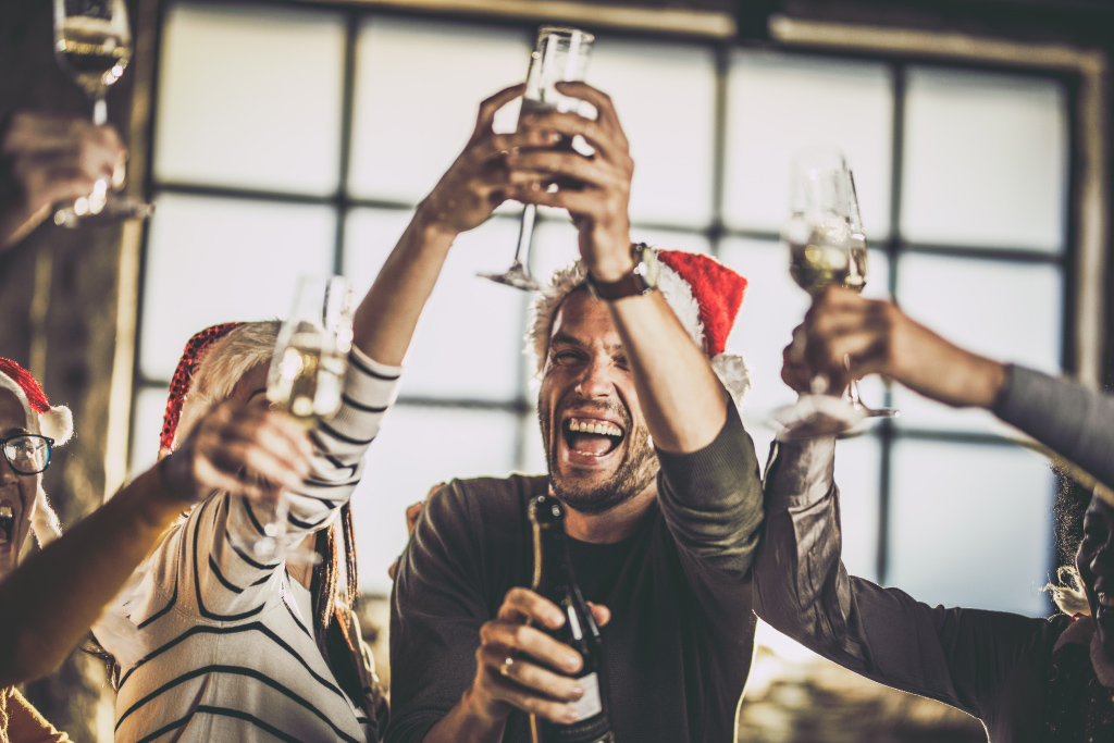 Kollegen mit Weihnachtsmützen stoßen mit Sekt im Büro an